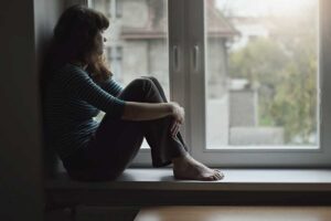 a person sits in a sill looking out of a window pondering the signs of addiction