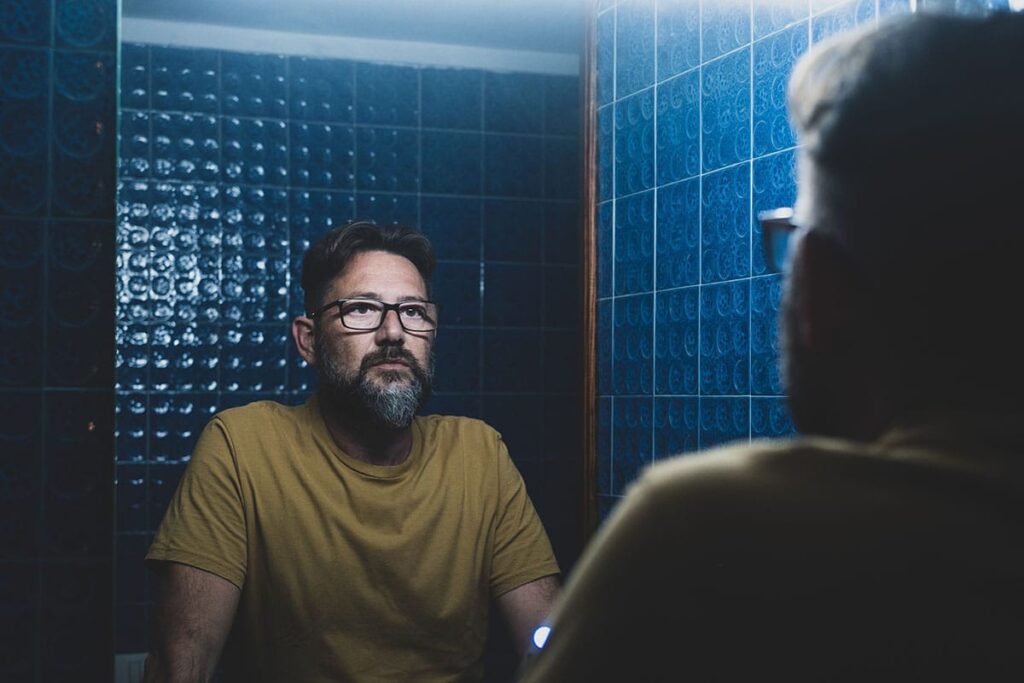 Man looking into mirror and thinking about the link between mental health and substance abuse